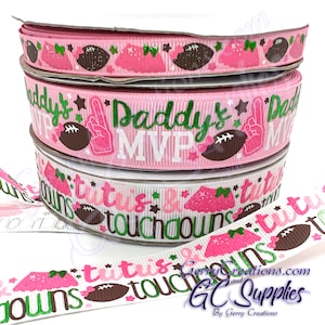 May include: Three spools of decorative ribbon with football-themed designs. The ribbons feature pink, white, and green colors with text that reads "Daddy's MVP" and "Tutús & Touchdowns". The ribbons also have football and tutu graphics.