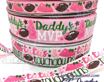 May include: Three spools of decorative ribbon with football-themed designs. The ribbons feature pink, white, and green colors with text that reads "Daddy's MVP" and "Tutús & Touchdowns". The ribbons also have football and tutu graphics.
