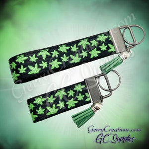 May include: Two black and green keychains with a green glitter leaf design and a green tassel. The keychains have a silver metal key ring.