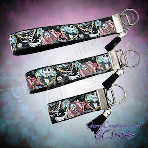 May include: Three black keychains with silver key rings and black tassels. Each keychain features a colorful printed design of Jack Skellington and Sally from the Nightmare Before Christmas.