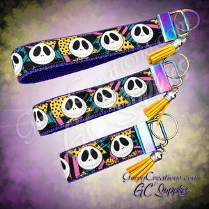 May include: Three colorful keychains with a black and white pattern of Jack Skellington's face from the Nightmare Before Christmas. Each keychain has a purple, black, and yellow ribbon with a gold tassel and a silver key ring.