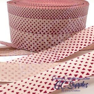 May include: A roll of beige ribbon with a repeating pattern of small red triangles. The ribbon is 1.5 inches wide and is perfect for crafting, gift wrapping, and decorating.