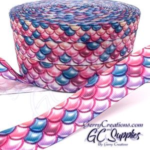May include: A roll of pink, blue, and white mermaid scale patterned ribbon. The ribbon is 1.5 inches wide and is perfect for crafting and decorating.