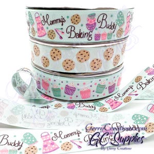 May include: Four rolls of light blue ribbon with different designs. The designs include cupcakes, chocolate chip cookies, and the text "Mommy's Baking" and "Buddy".