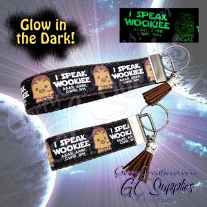May include: Two brown and black keychains with a cartoon image of a Wookiee. The keychains have a silver metal ring and a brown tassel. The text on the keychains reads "I Speak Wookiee Aaar, Arrr, Gww. Wh".
