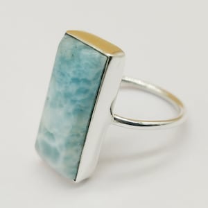 May include: A silver ring with a light blue rectangular gemstone set in a silver bezel. The ring has a simple band.