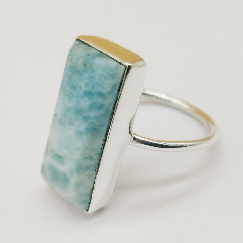 May include: A silver ring with a light blue rectangular gemstone set in a silver bezel. The ring has a simple band.