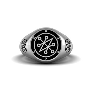 Könnte beinhalten: Ein silberner Siegelring mit einer schwarzen Emaille-Einlage, die ein weißes Symbol zeigt. Das Symbol ist ein stilisierter Stern mit fünf Zacken und acht Kreisen darum herum. Der Ring hat eine abgerundete ovale Form.