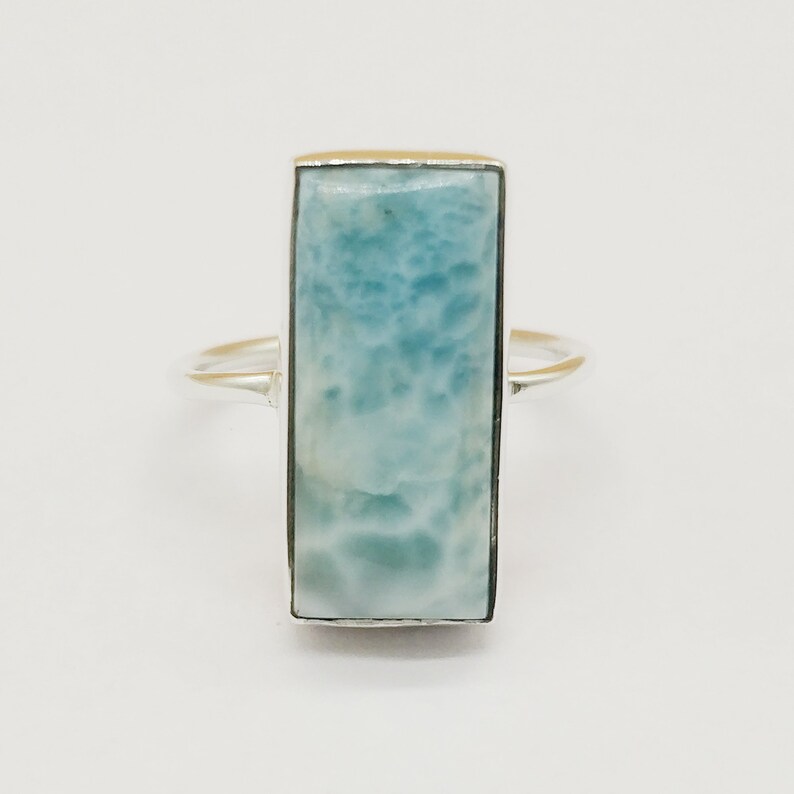 May include: A silver ring with a light blue rectangular gemstone. The gemstone has a cloudy, marbled pattern.