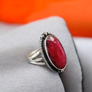 May include: A silver ring with a large, oval-shaped, red gemstone set in a silver bezel. The ring has a rope-like design around the bezel.