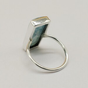 May include: A silver ring with a light blue rectangular gemstone set in a bezel setting.