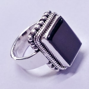 Puede incluir: Un anillo de plata con una piedra rectangular negra engastada en un engaste de plata. El engaste está decorado con un diseño de cuerda y pequeñas cuentas.