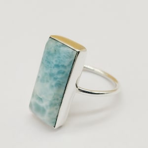 May include: A silver ring with a light blue, rectangular, gemstone. The gemstone has a cloudy, marbled pattern.