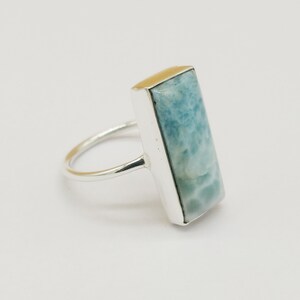 May include: A silver ring with a light blue rectangular gemstone. The gemstone has a marbled pattern.