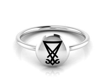 May include: A silver ring with a round, black sigil on the top. The sigil is a triangle with a cross inside.