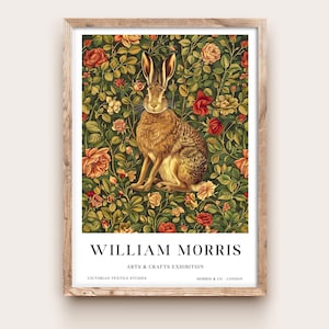 May include: A framed art print depicting a brown hare surrounded by a floral design of roses and leaves. The print includes the text "WILLIAM MORRIS ARTS & CRAFTS EXHIBITION" and "VICTORIAN TEXTILE STUDIES MORRIS & CO - LONDON". The artwork is in a wooden frame.