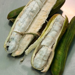 May include: Several ice cream bean pods, also known as Inga edulis, are shown with some split open to reveal the white, fluffy, fibrous pulp surrounding dark seeds inside. The outer husks are a textured, elongated green with brown stems.