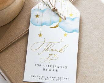 May include: A brown gift box with a pink ribbon and a thank you tag. The tag features a watercolor illustration of a blue cloud with a gold crescent moon and stars. The text on the tag reads "Thank you for celebrating with us! Samantha's Baby Shower January 17, 2021."