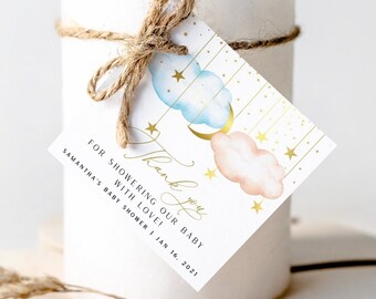 May include: White candle with a thank you tag tied around it. The tag features a blue and pink watercolor cloud design with gold stars and a crescent moon. The text on the tag reads "Thank you for showering our baby with love! Samantha's Baby Shower | Jan 14, 2021".