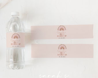 Op de afbeelding: Twee roze en bruine waterfleslabels met een regenboog en een bloemenpatroon. De tekst op de labels luidt "Gracie's First Birthday 01.28.2023".