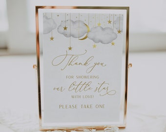May include: A white sign with gold lettering in a gold frame. The sign says "Thank you for showering our little star with love! Please take one". The sign has a watercolor illustration of clouds, stars, and a crescent moon.