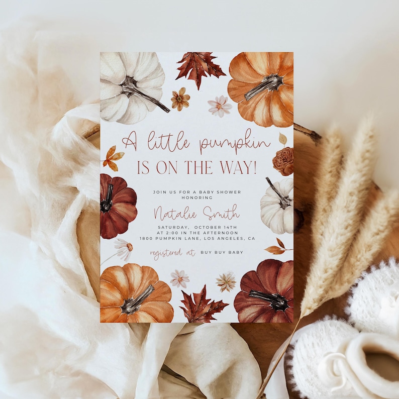 Pumpkin baby shower invitation with orange, copper and white pumpkin and autumn florals and leaves placed on a chair.