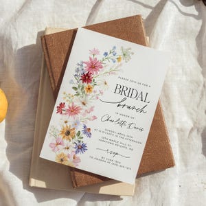 Bridal shower invitation with colorful wildflowers arch and cursive writing. The invite includes watercolor illustration of soft summer wildflowers in pink, yellow, blue, purple, red and white tones. The text includes bridal brunch as it's title.