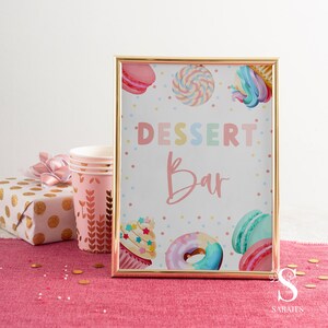 May include: A gold framed sign with a white background and colorful polka dots. The sign says "Dessert Bar" in rainbow letters with a pink cupcake, donut, and macarons.