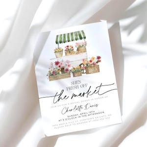 Pu&ograve; includere: Un biglietto d'invito bianco con un'illustrazione ad acquerello di un carretto di fiori. Il carretto ha una tenda a strisce verdi e bianche ed &egrave; pieno di fiori colorati. Il testo recita "She's Fresh Off the Market" e i dettagli per un addio al nubilato.