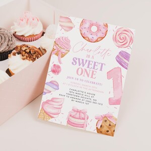 Pode incluir: Um convite de festa de primeiro aniversário rosa e roxo com uma ilustração em aquarela de um donut, um cupcake, um cone de sorvete, uma pirulito e um macaron. O texto do convite diz "Charlotte is a Sweet One" e inclui detalhes sobre a festa, como a data, a hora e o local.