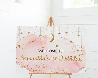 May include: A pink and gold welcome sign with a crescent moon and stars. The sign says "Welcome to Samantha's 1st Birthday".