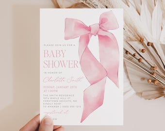 Puede incluir: Una invitación de baby shower rosa con una ilustración de acuarela de un lazo rosa. El texto de la invitación dice "Por favor, únase a nosotros para una baby shower en honor a Charlotte Smith, domingo 25 de enero a la 1:00 pm. The Smith Residence, 1974 Maple Hill St, Yorktown Heights, ND. Por favor, confirme su asistencia a Amanda (555) 555-1212. Registrado en..."