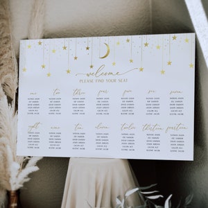 May include: A white seating chart with gold stars and a crescent moon. The chart is titled "Welcome, Please Find Your Seat." and lists names for each table number from one to fourteen.