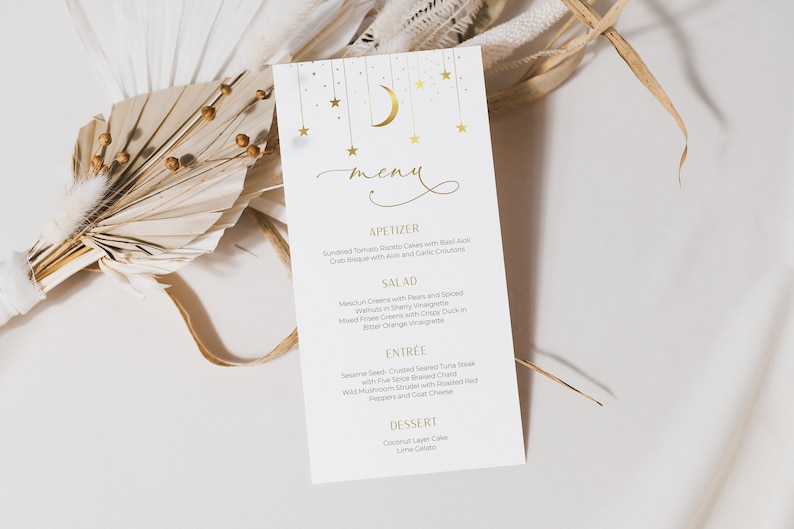 Op de afbeelding: Een witte menukaart met een gouden halve maan en sterrenontwerp. Het menu bevat opties voor voorgerechten, salade, hoofdgerecht en dessert. De tekst op het menu is in goud.