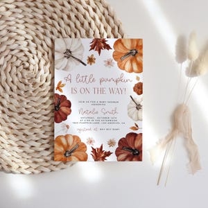 Pumpkin baby shower invitation with orange, copper and white pumpkin and autumn florals and leaves placed on a boho table.