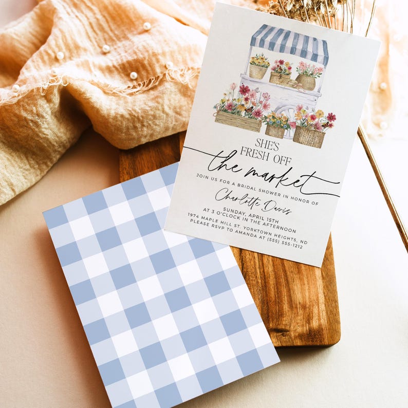 Op de afbeelding: Een witte uitnodiging met een blauw-wit geruit patroon op de achterkant. De uitnodiging is voor een bruidsdouche voor Charlotte Davis. De uitnodiging zegt "She's Fresh Off the Market" en heeft een aquarel-illustratie van een bloemenkraam.