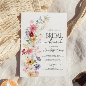 Bridal shower invitation with colorful wildflowers arch and cursive writing. The invite includes watercolor illustration of soft summer wildflowers in pink, yellow, blue, purple, red and white tones. The text includes bridal brunch as it's title.