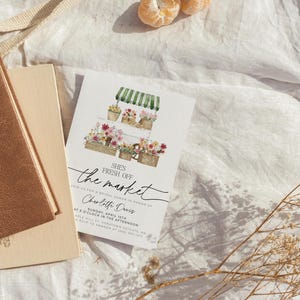 Pu&ograve; includere: Un invito per un addio al nubilato con un'illustrazione ad acquerello di una bancarella del mercato dei fiori. Il testo recita "She's Fresh Off the Market" e include il nome della sposa, la data, l'ora e il luogo.