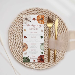 Puede incluir: Tarjeta de menú de cena de Acción de Gracias con calabazas de acuarela y hojas de otoño. El menú incluye aperitivos, platos principales, postres y bebidas. Tenedor y cuchillo dorados con una cinta beige sobre un salvamanteles tejido.