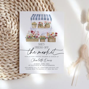 Op de afbeelding: Een aquarel-illustratie van een bloemenkar met een blauw-wit gestreept luifel. De tekst "SHE'S FRESH OFF the market" is geschreven in zwarte cursieve letters. De tekst "JOIN US FOR A BRIDAL SHOWER IN HONOR OF Charlotte Davis" is geschreven in zwarte letters. De tekst "SUNDAY, APRIL 15TH AT 3 O'CLOCK IN THE AFTERNOON 1974 MAPLE HILL ST. YORKTOWN HEIGHTS, ND PLEASE RSVP TO AMANDA AT (555) 555-1212" is geschreven in zwarte letters.