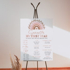 Puede incluir: Un póster imprimible para los hitos del primer año de un bebé, con un arcoíris rosa y marrón y un borde de hojas. El póster incluye el nombre del bebé, Samantha, la fecha de nacimiento, el peso, la altura y otros hitos del primer año.