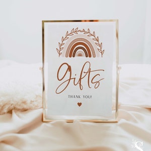 May include: A gold-framed sign with a white background and a brown rainbow design. The sign says "Gifts" in cursive with the words "Thank You!" below. A small heart is at the bottom of the sign.