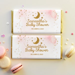 Peut inclure: Deux emballages de barres chocolatées roses et blanches avec des accents dorés. Les emballages présentent un fond aquarelle avec des paillettes dorées et une lune croissante dorée et des étoiles. Le texte sur les emballages indique "Baby Shower de Samantha 15 décembre 2020".