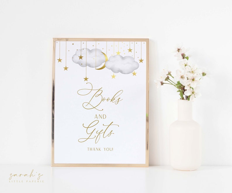 May include: A white sign with gold lettering and a gold crescent moon and stars graphic. The sign reads "Books and Gifts Thank You!"