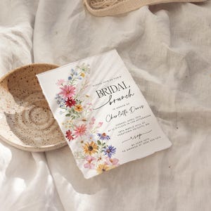 Bridal shower invitation with colorful wildflowers arch and cursive writing. The invite includes watercolor illustration of soft summer wildflowers in pink, yellow, blue, purple, red and white tones. The text includes bridal brunch as it's title.