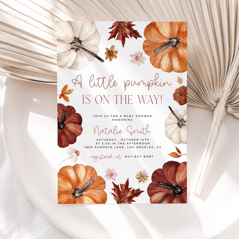 Pumpkin baby shower invitation with orange, copper and white pumpkin and autumn florals and leaves placed on a table.