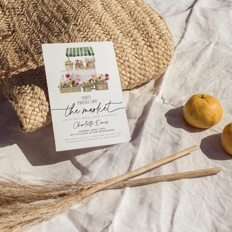 Pu&ograve; includere: Un biglietto d'invito bianco con il testo "She's Fresh Off the Market" e illustrazioni floreali. Il biglietto &egrave; appoggiato su una borsa di paglia intrecciata e tessuto bianco, con arance e bastoncini di legno nelle vicinanze. L'invito &egrave; per un addio al nubilato.
