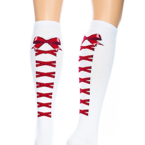 May include: White knee-high socks with a red ribbon and criss-cross design. The socks feature a red bow at the top and a series of red criss-cross laces down the front. The socks are made of a soft, comfortable material.