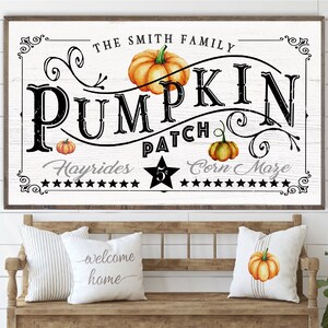May include: A white sign with black lettering that reads "The Smith Family Pumpkin Patch Hayrides $5 Corn Maze". The sign is decorated with a pumpkin and fall leaves.