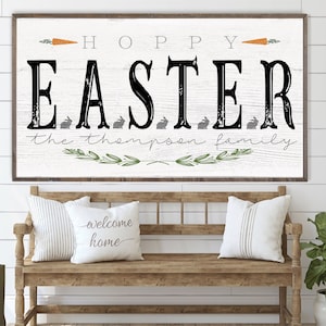 May include: White wooden sign with black text that reads "Hoppy Easter the Thompson family". The sign has a rustic look and is decorated with green leaves and orange carrots.
